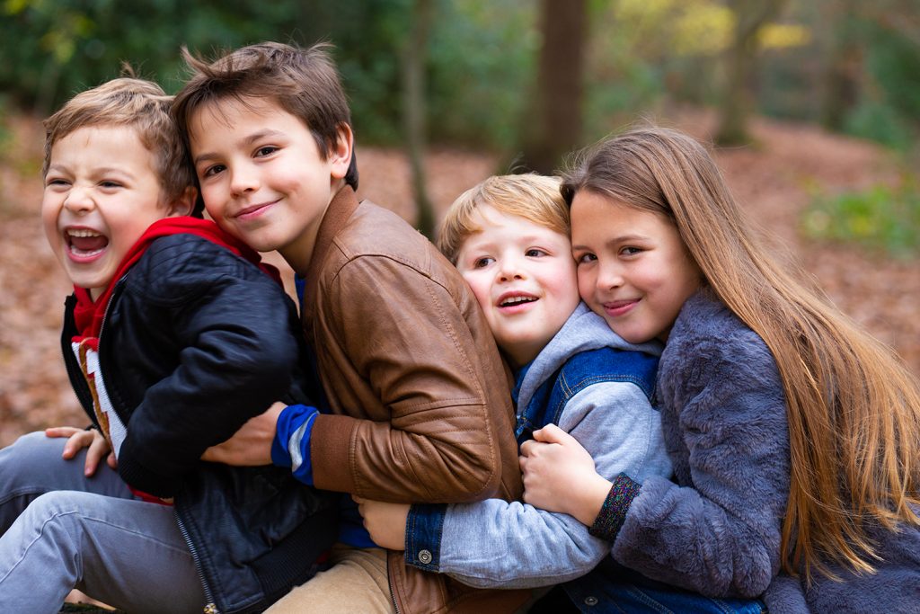 Four brothers and sisters hugging in the woods and laughing