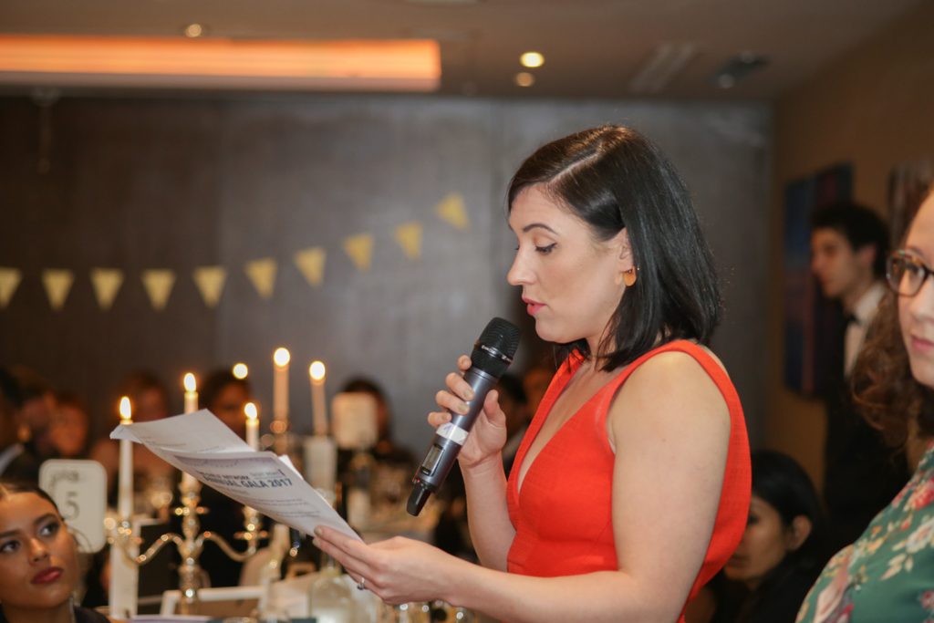 Woman in red dress making speech at gala dinner