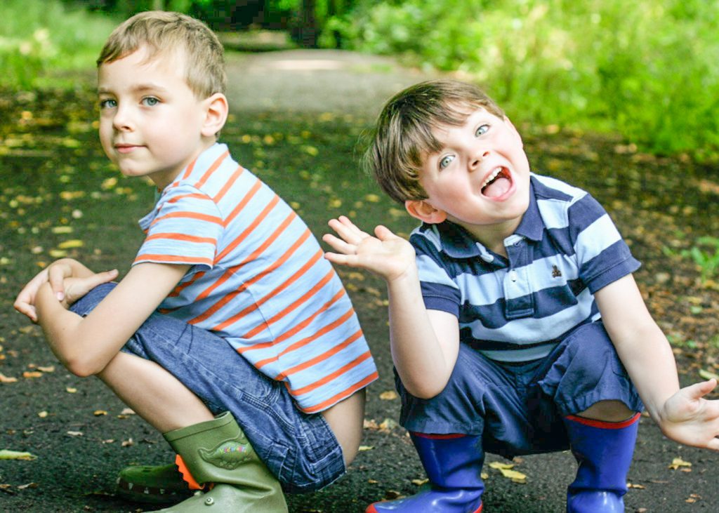 young brothers in wellington boots crouching down in the garden