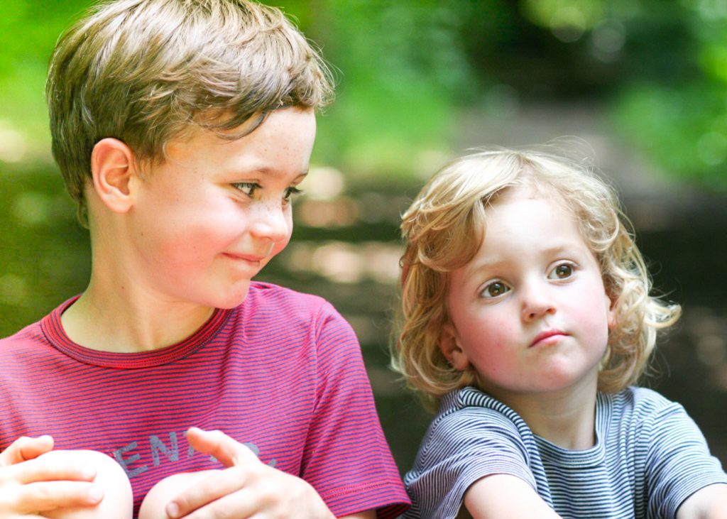 Older brother smiling down at his little brother while sitting in the woods
