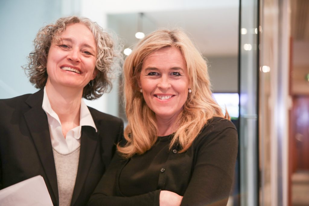 Two corporate women standing in an office and laughing into the camera