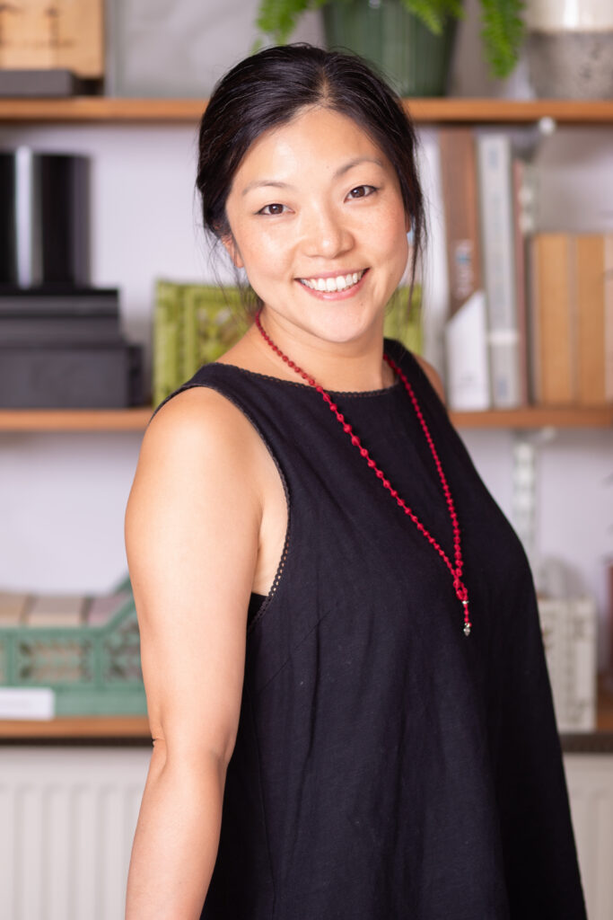 Pretty Asian woman in black dress with red necklace standing in office