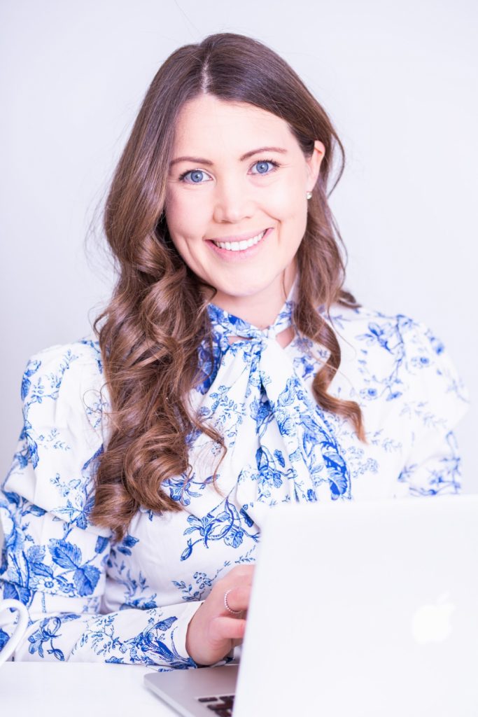 Woman with long brown hair and flowery blouse sitting at her laptop