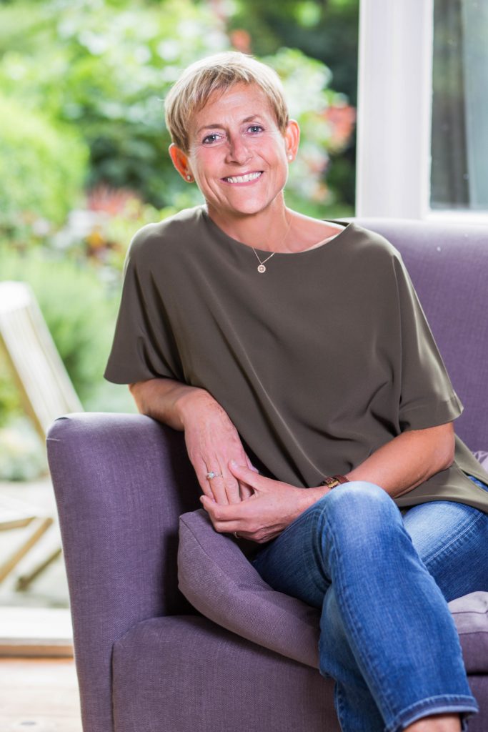 Friendly woman sitting on purple sofa in front of French doors leading to garden