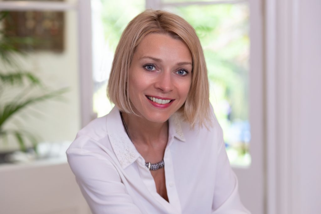 beautiful woman sitting in front of French doors smiling at camera wearing white shirt