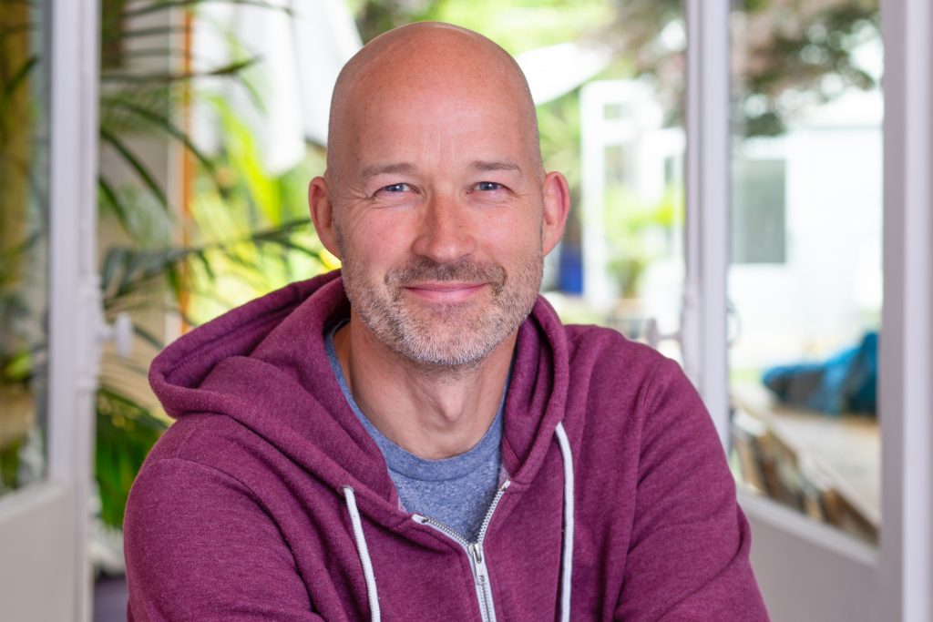 Man in hoodie smiling in front of French doors