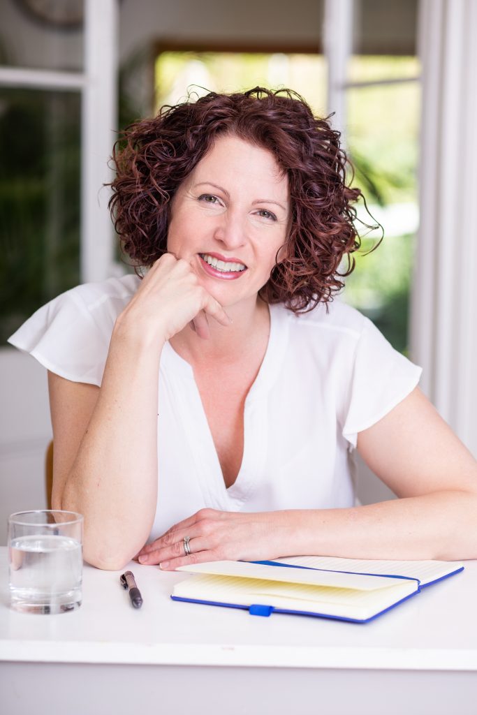 Woman with warm smile sitting at desk with notebook and pen