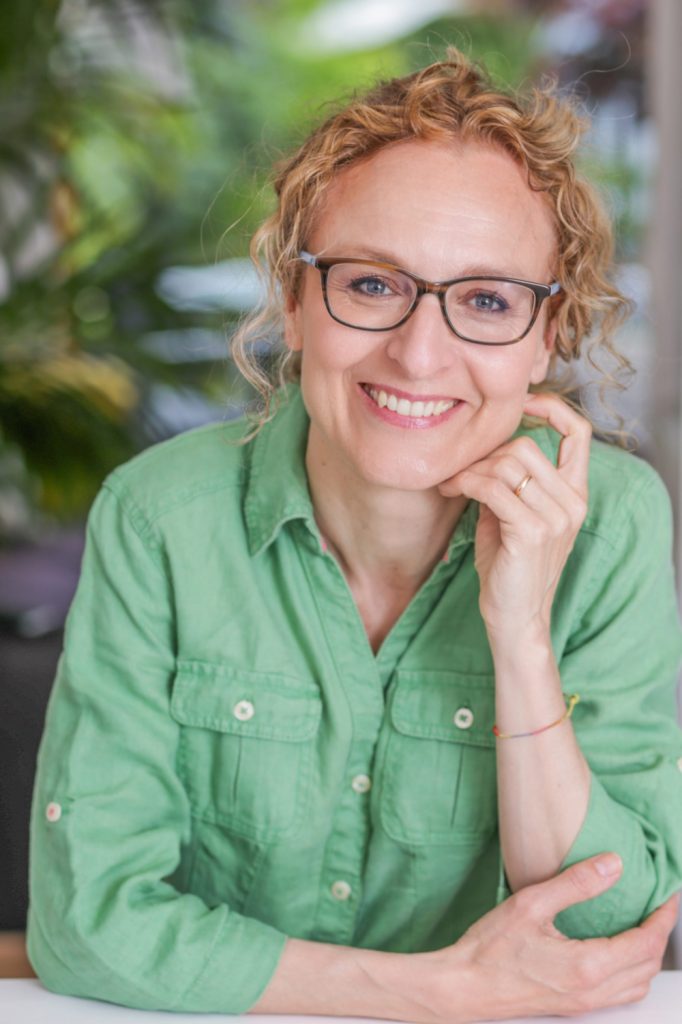 Kind looking woman in green shirt smiling warmly into the camera