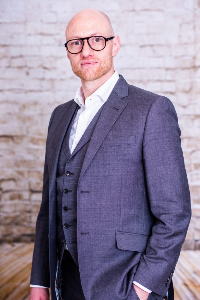 Smart man in glasses and blue suit standing in front of white brick wall
